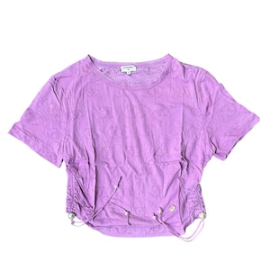 May include: A lavender-colored, short-sleeved crop top with a round neckline. The shirt features an all-over floral eyelet pattern and drawstring details on the sides. The brand name "CHANEL" is visible on the tag.