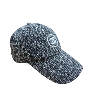 Op de afbeelding: Een zwart-witte tweed baseballcap met een gebogen klep. De pet heeft een wit geborduurd logo op de voorkant. Een klassiek accessoire.