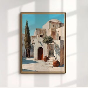 Puede incluir: Una pintura enmarcada representa una escena de un pueblo mediterráneo soleado. La obra presenta edificios blancos con puertas arqueadas, un techo abovedado y macetas de terracota. Un árbol alto y delgado se alza a la izquierda, con un cielo azul claro arriba.
