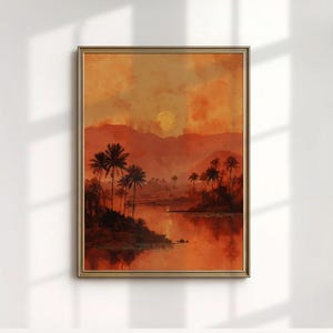 May include: Framed art print of a tropical sunset scene. The artwork shows palm trees, mountains, and a golden sun reflected in a river, rendered in warm orange and red tones. The print is in a gold-coloured frame.