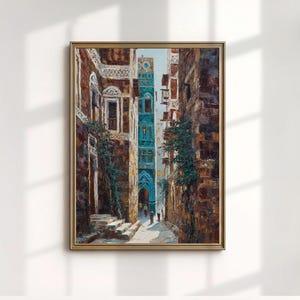May include: A framed oil painting depicts a narrow street scene with tall, aged buildings. The buildings are primarily brown with a turquoise archway and accents. The artwork has a gold frame and is displayed against a white wall.