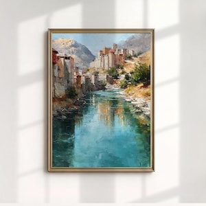 May include: A framed landscape painting depicts a river flowing through a valley with a village on the hillside. The artwork features a palette of blues, browns, and greens, with a gold-colored frame. The painting evokes a sense of tranquility and natural beauty.