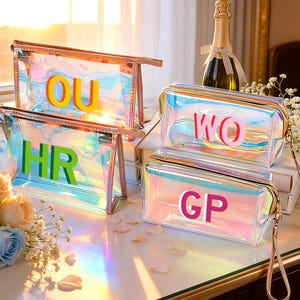 May include: Four iridescent cosmetic bags with gold-toned frames and wrist straps. Each bag has a different set of colorful letters: OU, HR, WO, and GP. The bags sit on a white surface with flowers and a champagne bottle in the background.