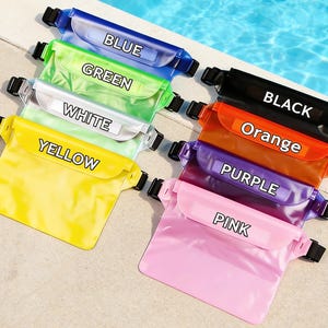 Op de afbeelding: Een verzameling waterdichte heuptassen in verschillende kleuren, waaronder blauw, groen, wit, geel, zwart, oranje, paars en roze. Elke tas heeft een zwarte verstelbare riem en de kleurnaam staat erop.