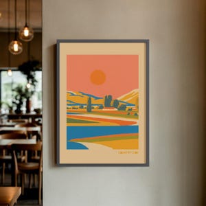 Könnte beinhalten: Gerahmter Kunstdruck mit einer stilisierten Landschaftsszene. Das Kunstwerk zeigt eine lebendige Farbpalette mit einem orangefarbenen Himmel, einer gelben Sonne und Feldern in Blau, Grün und Gelb. Das Wort "COUNTRYSIDE" ist unten aufgedruckt.