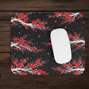 May include: A black mouse mat with a floral pattern of red flowers and white branches. A white computer mouse sits on the mat. The design is repeated across the surface.
