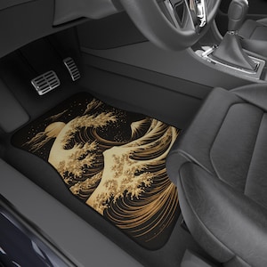 May include: Car floor mat featuring a Japanese wave design in shades of gold and black. The artwork depicts a large wave with a setting sun and clouds. The mat is rectangular and fits in the driver's side footwell of a car.