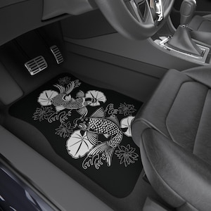 以下が含まれることがあります： 黒い車のフロアマット。白い鯉と蓮の花のデザインが施されています。マットは長方形で、車の足元にフィットします。デザインは、魚と花の詳細なイラストです。