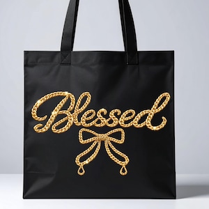 Puede incluir: Bolso tote negro con la palabra "Blessed" en letras doradas con forma de cadena y un diseño de lazo dorado. El bolso tiene dos asas negras y está hecho de un material liso y mate. El diseño está centrado en la parte delantera.
