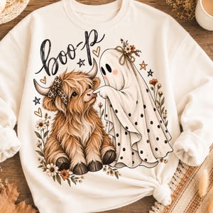 Puede incluir: Una sudadera de cuello redondo color crema con un estampado gráfico de una vaca highland marrón y peluda con un lazo de estampado de leopardo y un fantasma blanco con lunares negros. El fantasma toca la nariz de la vaca. El texto "boo-p" está impreso arriba.