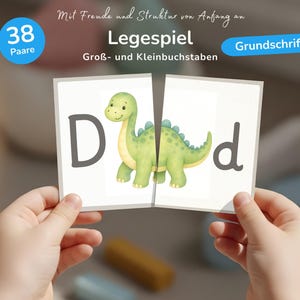 K&ouml;nnte beinhalten: Ein Legespiel mit 38 Paaren aus Karten, die Gro&szlig;- und Kleinbuchstaben sowie eine gr&uuml;ne Dinosaurier-Illustration zeigen. Die Karten enthalten den Text Mit Freude und Struktur von Anfang an, Legespiel, Gro&szlig;- und Kleinbuchstaben, Grundschrift.