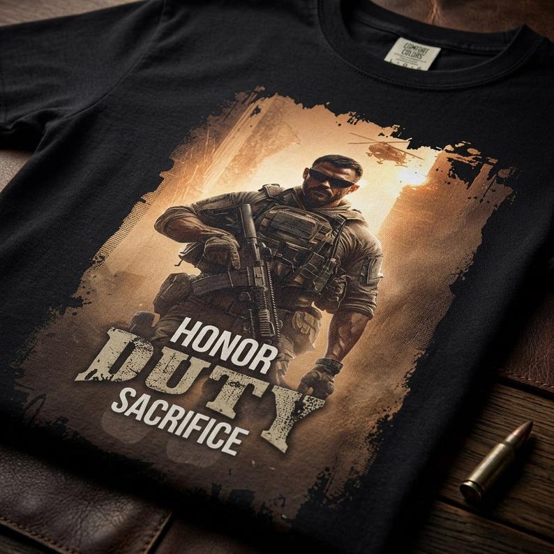 May include: A black t-shirt featuring a graphic print of a soldier in tactical gear holding a rifle. The soldier wears sunglasses and a vest. Above the soldier, a helicopter is visible. The text HONOR DUTY SACRIFICE is printed in white.