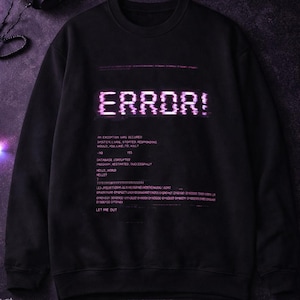 Peut inclure: Sweat-shirt noir avec le mot "ERROR!" en lettres roses pixélisées. Le design comprend des lignes de code et la phrase "LET ME OUT". Le haut a un col rond et des manches longues.