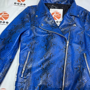 May include: A bright blue motorcycle jacket featuring a black snakeskin-like pattern, a silver-toned asymmetrical zipper, two zippered side pockets, and a notched collar. The interior label displays the text ana plus with social media icons.