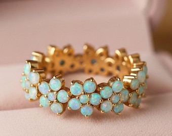 May include: A gold ring with a floral design, featuring small, light blue opal stones. The ring is set in a gold band and is displayed in a pink jewelry box.
