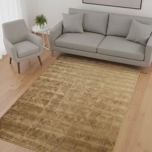 Könnte beinhalten: Ein Wohnzimmer mit einem rechteckigen, goldbraunen Teppich mit geometrischem Dreieckmuster. Der Teppich liegt auf einem Holzboden, mit einem grauen Sofa, einem Sessel und einem kleinen Beistelltisch mit einer Pflanze. Ein abstraktes Kunstwerk hängt an der Wand.