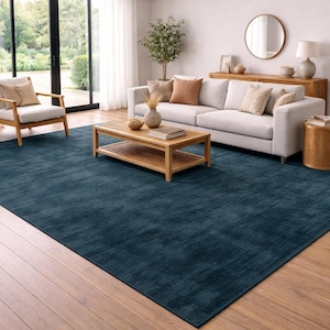 Peut inclure: Un grand tapis rectangulaire bleu foncé dans un salon. Le tapis est posé sur un parquet, avec un canapé, une chaise et une table basse. La pièce bénéficie de la lumière naturelle et d'une palette de couleurs neutres.