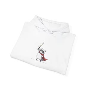 Puede incluir: Sudadera con capucha blanca con un personaje de mapache de dibujos animados que lleva una capa roja y sostiene una espada. El mapache tiene una máscara negra y una bufanda roja. La sudadera tiene una capucha con cordón.