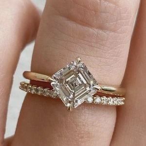 May include: A gold engagement ring with a large, square-cut diamond as the centerpiece. A smaller, gold band with small diamonds sits below it. The rings are on a finger.
