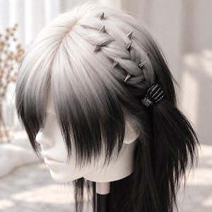 May include: A synthetic wig featuring a white-to-black ombre color transition with straight bangs. The hair is styled with a side braid adorned with silver-toned metal spikes and secured with a black skeletal hand-shaped hair clip on a mannequin.