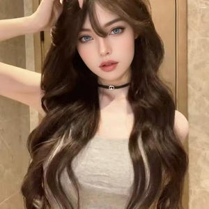 Op de afbeelding: Een persoon met lang, golvend bruin haar met blonde highlights en blauwe ogen. Ze draagt een grijze tube top en een zwarte choker ketting.