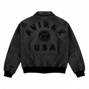Puede incluir: Chaqueta bomber de cuero negro con la palabra "AVIREX" arqueada en la espalda, encima de un emblema circular y la palabra "USA". La chaqueta tiene cuello, pu&ntilde;os y dobladillo de canal&eacute;.