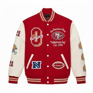 Puede incluir: Chaqueta universitaria roja y crema con el logo y texto de los 49ers de San Francisco. Cuenta con parches con el número 21, cascos de fútbol y el texto "October's Very Own". La chaqueta tiene puños y cuello a rayas.
