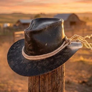 May include: A dark brown, weathered cowboy hat with a distressed finish and a pinched crown. The hat features a thick, light-colored braided rope hatband that wraps around the base of the crown and ties into a knot on the side with loose ends.