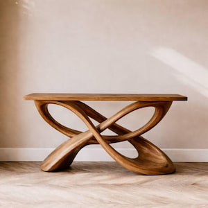 May include: A wooden console table with a distinctive, sculptural design. The table has a rectangular top supported by intertwined, flowing wooden curves. The natural wood grain is visible, and the table is finished with a light stain. The overall aesthetic is modern and artistic.