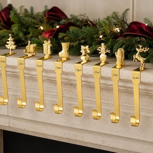 Può includere: Un set di nove ganci portacalza in metallo color oro, ognuno caratterizzato da un topper a tema natalizio unico tra cui un fiocco di neve, albero, slitta, regalo, calza, campana, pupazzo di neve, guanto, renna e ghirlanda, con nomi incisi.