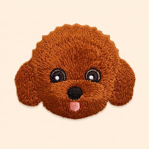 Op de afbeelding: Een bruine geborduurde patch met de kop van een hond met krullend haar. Het ontwerp bevat donkerbruine ogen met witte accenten, een zwarte neus en een klein roze tongetje dat uit de mond steekt, alles uitgevoerd in dicht borduurwerk.