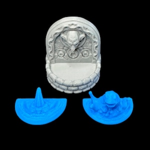 May include: A gray miniature fountain with an elephant head design, and two blue, semi-circular pieces. The fountain has a stone-like texture and a circular basin. The blue pieces appear to be water features.