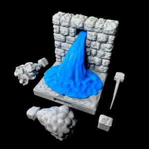 May include: A miniature fantasy scene featuring a stone wall with a blue waterfall. The scene includes several gray stone-like elements, including two decorative pieces, a hammer, and a small square block. The background is black.