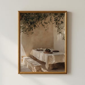 Może przedstawiać: Oprawiony wydruk przedstawia scenę obiadu na świeżym powietrzu. Stół jest nakryty talerzami i miską z owocami, przykryty białym obrusem. Kamienna ławka stoi przed stołem, a gałęzie oliwne zwisają nad nim. Rama jest złota.