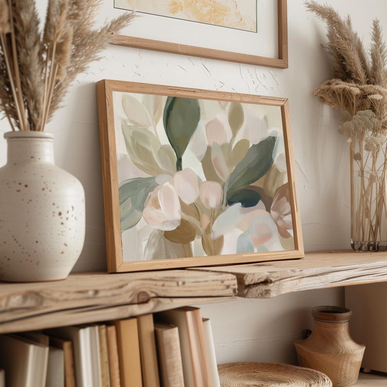 May include: A framed abstract floral painting in a wooden frame. The artwork features soft, muted colours including shades of green, pink, and beige. The painting is displayed on a rustic wooden shelf, alongside a vase with dried plants and a ceramic vase.