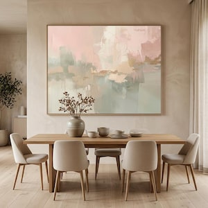 May include: A dining room scene featuring a large abstract painting in soft pinks, greens, and gold tones. A wooden dining table is surrounded by beige upholstered chairs. A vase with dried branches sits on the table.