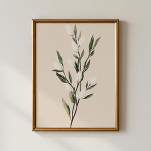 Puede incluir: Una impresión botánica enmarcada que presenta una rama de flores blancas y esponjosas y hojas verdes sobre un fondo beige. La obra de arte está encerrada en un marco dorado, creando una estética clásica y elegante. Adecuado para la decoración del hogar.