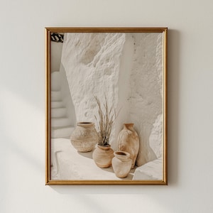 Puede incluir: Una impresión enmarcada que presenta una pared blanca texturizada y soleada con un conjunto de jarrones de cerámica decorativos. Los jarrones son de varios tamaños y formas, con una paleta de colores neutros. Algunos jarrones contienen hierbas secas, creando una estética minimalista y bohemia.