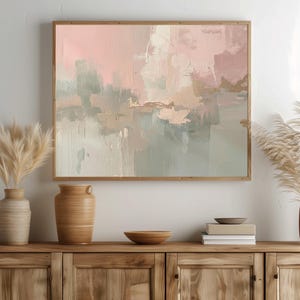 May include: Abstract art print in a wooden frame. The artwork features a blend of pink, beige, and gray brushstrokes with gold accents. The painting is displayed above a wooden cabinet with decorative vases and bowls.