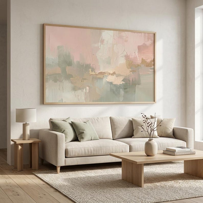 May include: Large abstract painting in a wooden frame, featuring soft pink, green, and beige brushstrokes. The artwork hangs above a beige sofa with green and beige pillows. A wooden side table with a lamp and a coffee table complete the living room setting.