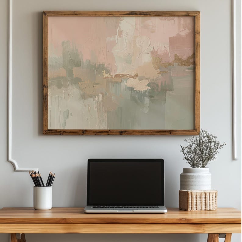 May include: Abstract art print in a wooden frame, featuring soft pink, beige, and green brushstrokes. A laptop with a blank screen sits on a wooden desk, along with a white vase and pencils.