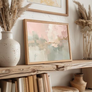 May include: Abstract art print in a wooden frame. The artwork features a blend of pink, green, and beige brushstrokes. The framed art is displayed on a rustic wooden shelf, alongside a ceramic vase with dried plants and a glass vase.