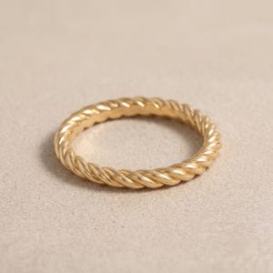 Könnte beinhalten: Ein goldener Ring mit einem durchgehenden gedrehten Seildesign. Das Band hat eine polierte metallische Oberfläche mit einer gleichmäßigen kreisförmigen Form und zeigt eine detaillierte Spiralstruktur, die den gesamten Umfang umschließt.