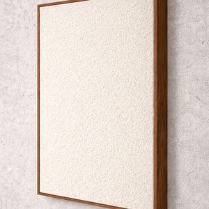 Puede incluir: Obra de arte mural rectangular con una superficie texturizada de color crema enmarcada por un borde de madera oscura. La obra está montada sobre una pared de hormigón gris claro.
