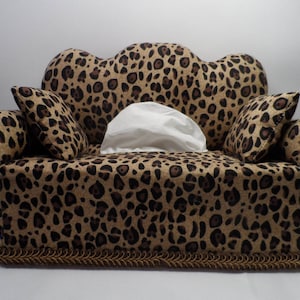 May include: A leopard print tissue box cover shaped like a sofa with two pillows and a white tissue box inside.