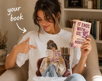 May include: A white t-shirt featuring a graphic of a person sitting in a maroon armchair reading a book titled It Ends With Us by Colleen Hoover. The shirt displays a bookshelf illustration behind the chair. The text your book is printed in white.