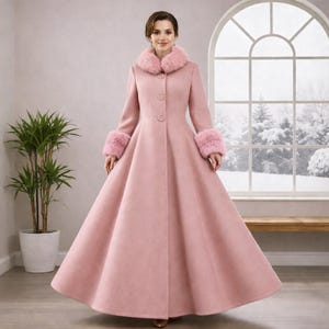 Puede incluir: Un abrigo largo de color rosa claro con falda acampanada y cuello y puños de piel sintética. El abrigo tiene tres botones en la parte delantera y un diseño clásico y elegante. El abrigo es largo hasta el suelo y parece estar hecho de un material suave.