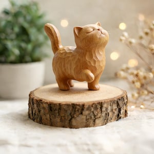 以下が含まれることがあります： 明るい色の木で彫られた、足を上げた状態で目を閉じた木製の猫の置物。 猫は、自然な樹皮の縁が付いた、小さくて丸い木の台座の上に立っています。 置物にはテクスチャ加工が施されています。