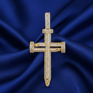 May include: A gold-colored cross pendant encrusted with numerous small, sparkling gemstones. The cross is set against a deep blue, textured background, creating a striking contrast. The pendant's design is detailed and ornate.