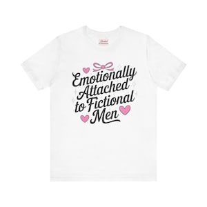 May include: White t-shirt featuring the phrase "Emotionally Attached to Fictional Men" in black script, decorated with pink hearts and a bow. A casual wear item.